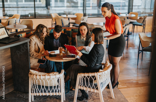 Obraz na plátně A diverse group of colleagues gathers around a small cafe table, reviewing a tablet and notes while enjoying drinks