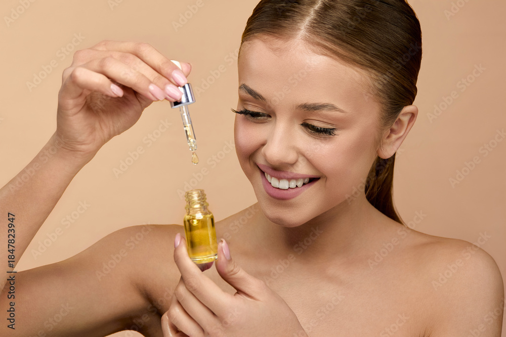 Fototapeta premium A young woman applies a serum with focus on her radiant skin, showcasing beauty techniques.