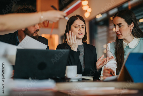 Bilde på lerret A tense meeting among colleagues around a cluttered table with laptops and papers; distressed gestures and focused faces convey disagreement and collaboration in a modern work environment