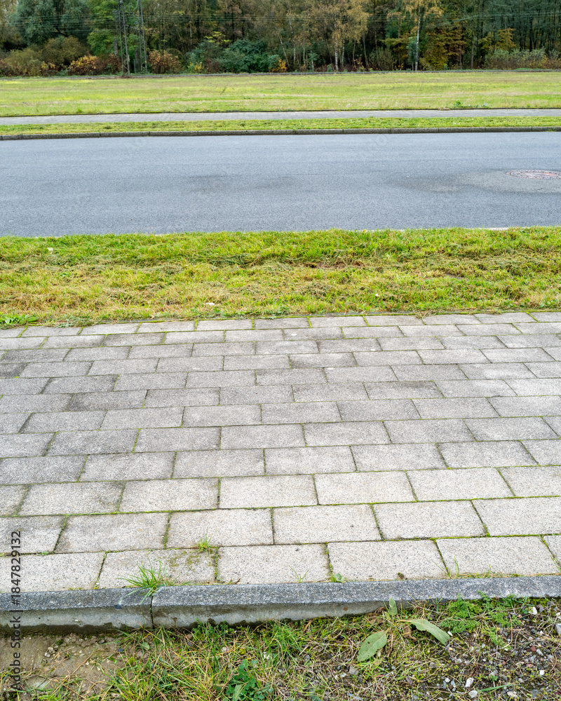 Obraz premium Paved sidewalk edges green grassy area along a road in a quiet rural setting during autumn season