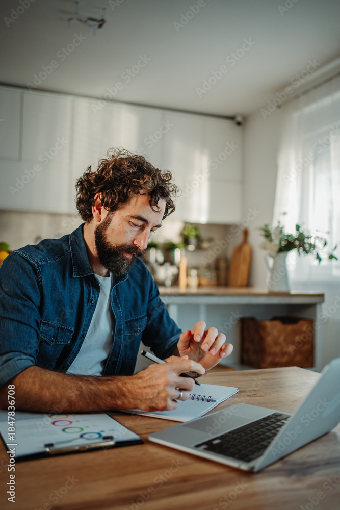 Fototapeta premium Man writing notes working from home kitchen