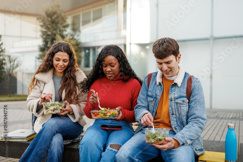 Tableau sur toile Diverse young people sitting outdoors, eating fresh salads and sharing a meal