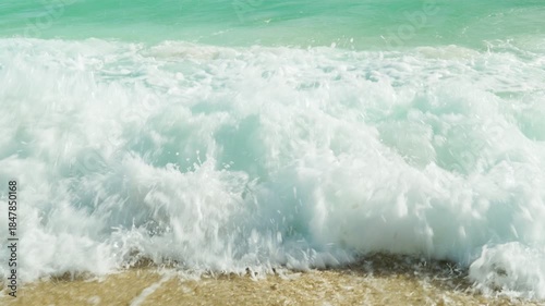 Seascape with coastal waves. Turquoise sea water with white foaming waves gently runs onto the sandy beach shore.
