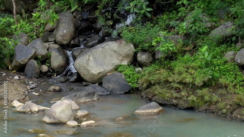 A small waterfall flowing into a river. A peaceful and calm atmosphere for relaxation. Ecological and environmental concepts. Realtime footage, 4K