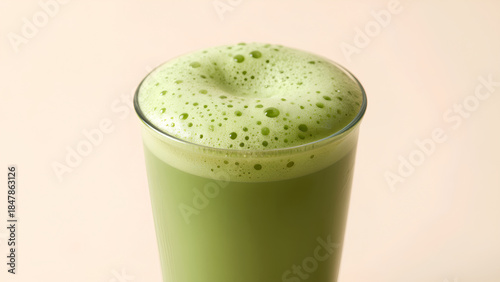 A vibrant green beverage with a frothy top, served in a clear glass against a soft background.