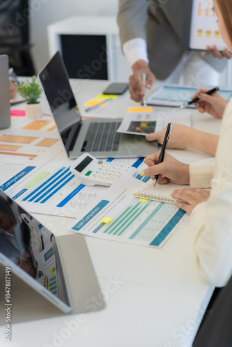 A close-up image shows the accounting team holding pens and pointing to graphs, analyzing marketing plans using calculators during a business brainstorming session.