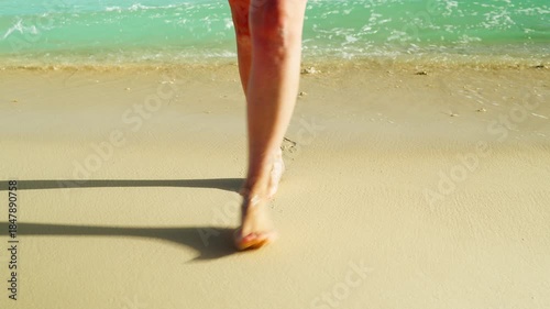 Slender female legs come out of the water on a sandy sea beach on a sunny day. A woman enjoys a vacation at sea. The concept of travel and tourism.