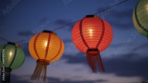 Glowing Asian paper lanterns hanging against twilight sky.