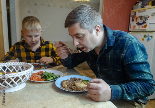 A man and his 9-year-old son eat together at the table