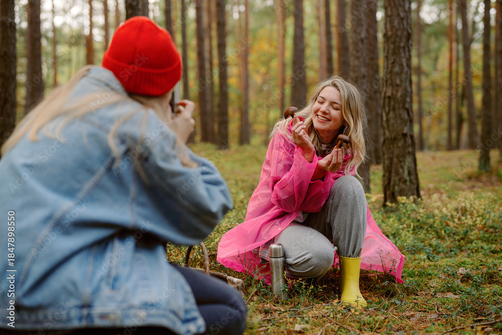 Fototapeta premium Two friends share a cheerful moment in a vibrant forest, dressed in playful outfits. Laughter fills the air as one captures the other’s joyful expression among the trees.