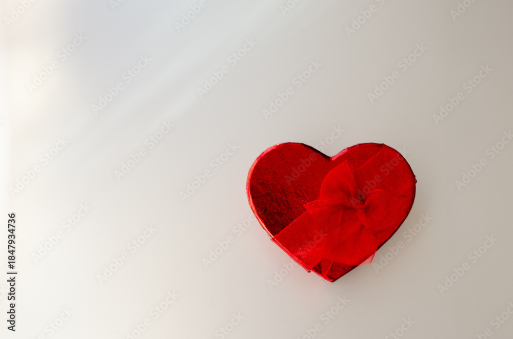 Fototapeta premium Minimalistic shot of red heart shaped gift box on matte gray background with a soft light and copy space