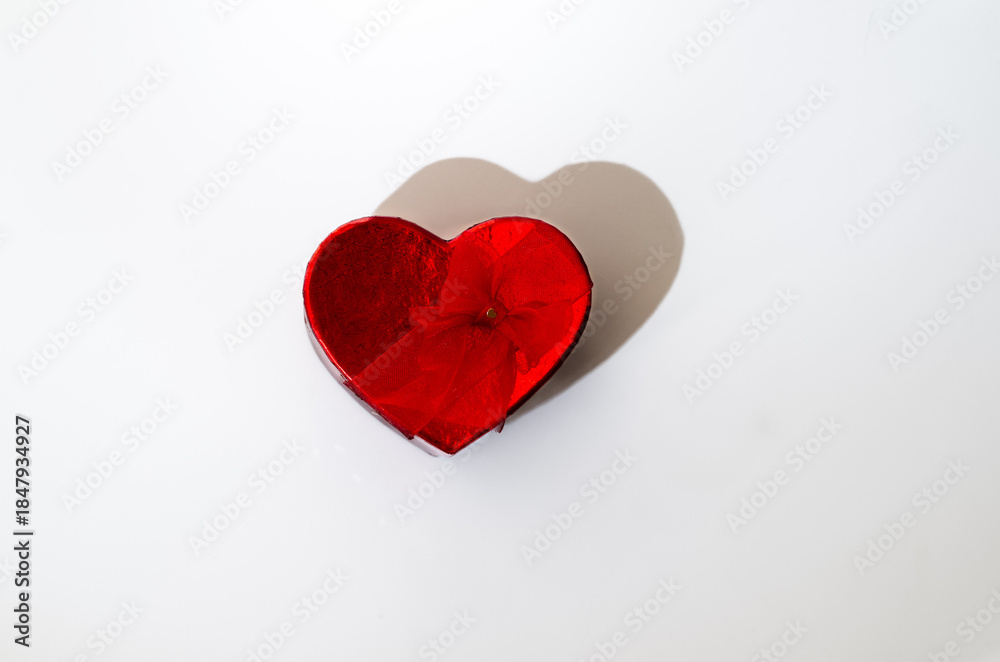 Fototapeta premium Red heart shaped gift box in center neutral background, hard dramatic shadow. horizontal minimalistic shot