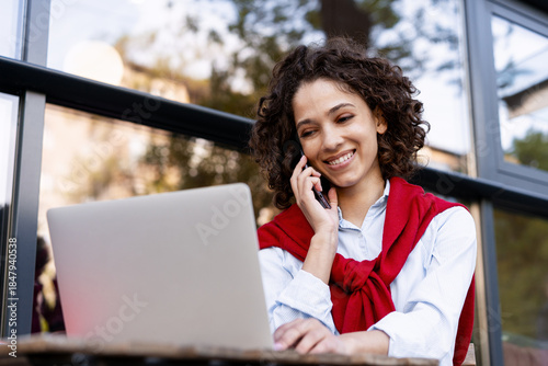 Foto Beautiful cheerful woman remote working, answering call using laptop outdoors
