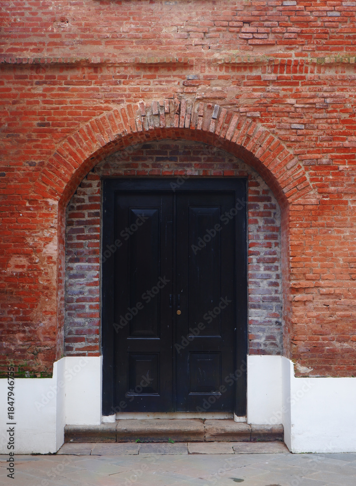Fototapeta premium Old wooden entrance door on a red brick wall. Old, antique, and historic building