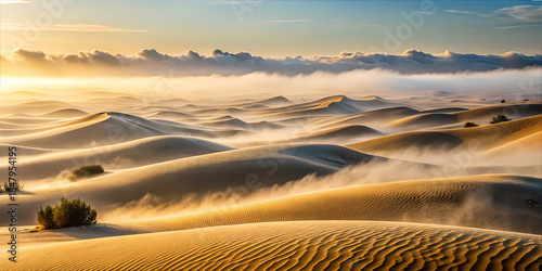 Sunrise over sand dunes with clouds and mist in a desert landscape during early morning light