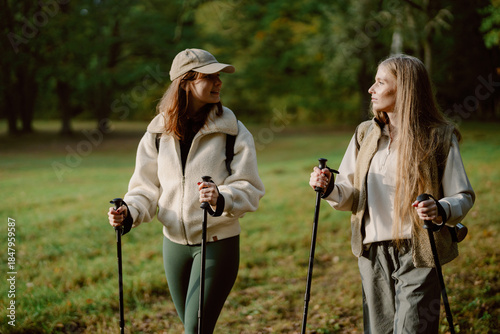 Картината върху платно Two women walk leisurely on a nature trail, holding trekking poles and chatting happily