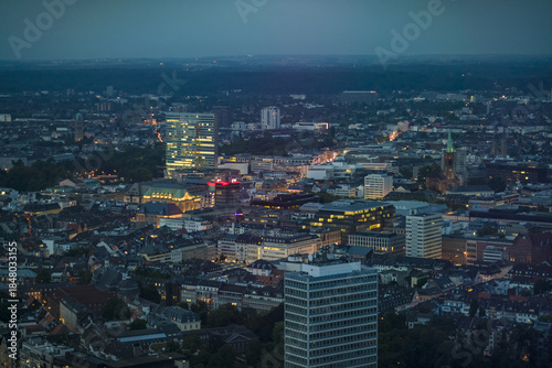 Aerial view of city lights twinkle across the cityscape, highlighting the modern architecture and historic church spires at dusk, Dusseldorf, North Rhine-Westphalia, Germany.