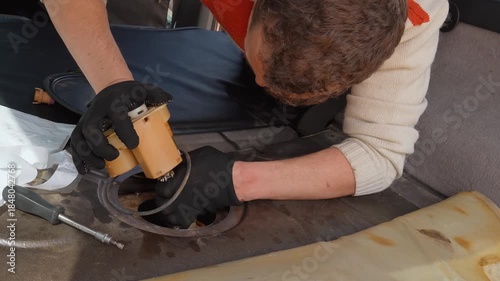 Car mechanic carefully replacing and installing a brand new fuel pump module into the gas tank of a modern vehicle during a maintenance and repair service at an auto garage workshop