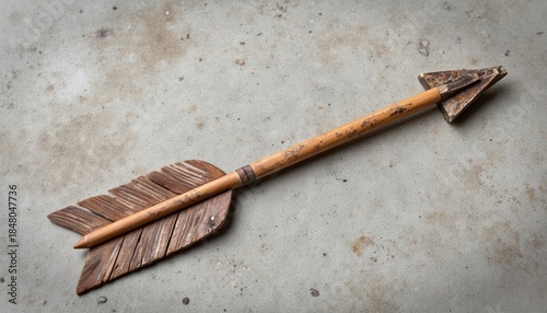 Wooden arrow with feather fletching lying on a concrete surface  