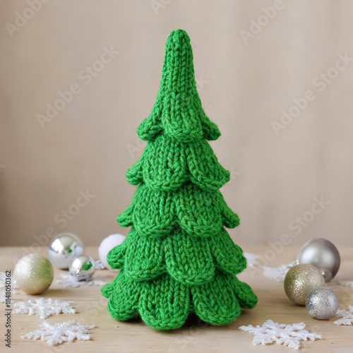 Knitted green Christmas tree with holiday ornaments and snowflakes on a wooden surface for winter festive decoration and seasonal celebration.