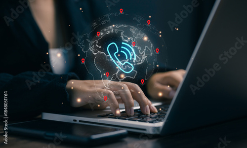 A professional types on a laptop with a global phone network hologram, representing VoIP communication, international call centers, customer service, telecom, and worldwide business connectivity.