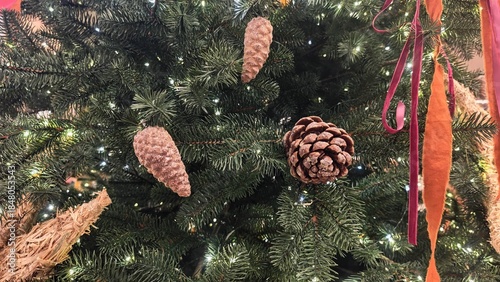 Close-up of a Christmas tree decorated with pine cones, glowing lights and colorful ribbons among green branches. Concept of natural holiday beauty, warmth and traditional festive atmosphere