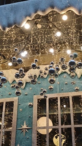 Shiny silver baubles and glowing lights decorate a winter-themed Christmas storefront with stars and snow. Concept of festive magic, holiday wonder and seasonal window display charm