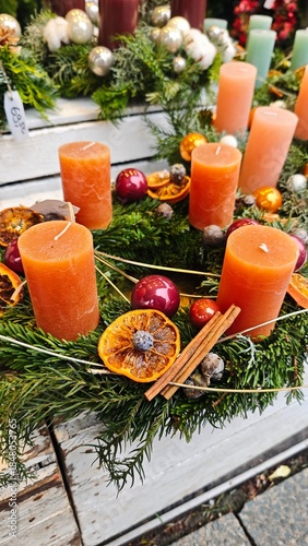 Christmas wreath with orange candles, dried citrus slices, cinnamon sticks and baubles on evergreen branches. Concept of warm holiday aroma, natural beauty and traditional seasonal charm