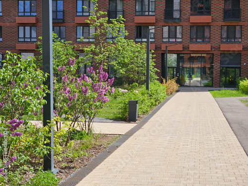 Brick building with a walkway in front of it. The walkway has a flower garden with purple flowers