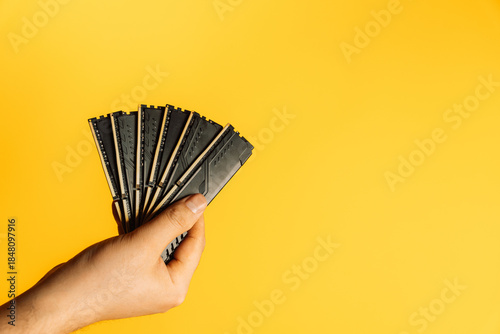 Photos Hand holding fan of black DDR RAM sticks on yellow background, upgrade concept