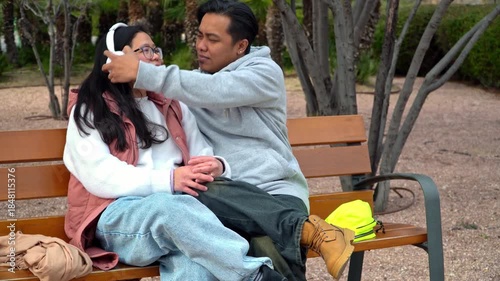 Asian couple listening music with headphones during a romantic date in the park