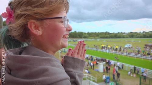 Overjoyed young girl enthusiastically claps her hands, her face lit up with a huge smile. She celebrates the victory of her favorite horse at the racetrack. A moment of pure happiness and success