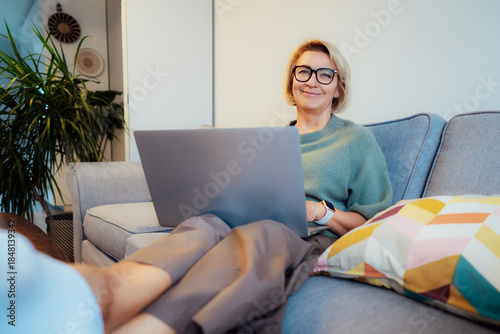Cozy remote job. Confident Mid aged woman self employed sit on sofa at home office workplace do accounting work for remote client, has online study. Small business entrepreneur manage business at home
