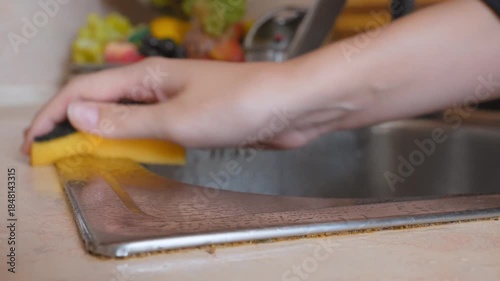 Female hand thoroughly cleans the dirty edge of the stainless steel kitchen sink with a yellow sponge, paying attention to household chores and maintaining hygiene in the house in the kitchen
