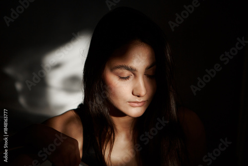 A woman with black hair wakes up in the morning in a white blanket and catches the rays of the sun. The portrait is creative, with brown eyes. High quality photo