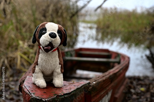 A stuffed dog sits on the stern of a boat on a small pond.