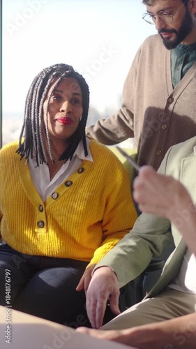 Vertical. Diverse group gathers around a screen for a collaborative discussion as a middle aged businesswoman leads conversation sharing ideas guiding colleagues during a strategy meeting at office