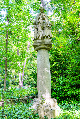 Pillar with religious figure of priest giving communion to children, park with representations of the seven sorrows of Mary, sunny day in Averbode, Scherpenheuvel-Zichem, Belgium