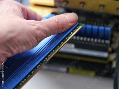 A man holding a computer RAM module with a large heat sink near a desktop motherboard.