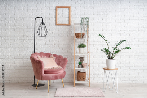 Interior of modern room with comfortable armchair, shelving unit and houseplants near white brick wall