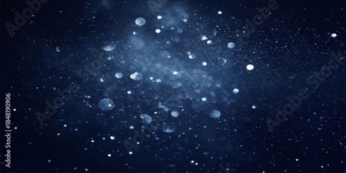 Glowing particles in the night sky resemble falling snow flakes and distant stars within a deep blue winter nebula of the starry cosmos universe