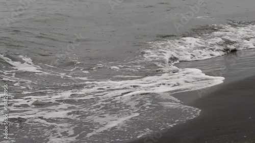 Moody close up shot of waves gently caressing a black volcanic sand beach. A serene yet striking backdrop perfect for mindfulness and reflection