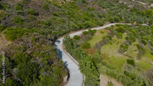 Cinematic Aerial Drone tracking shot of a car driving on a scenic coastal road in Zakynthos Greece overlooking the blue Ionian Sea and green rolling hills