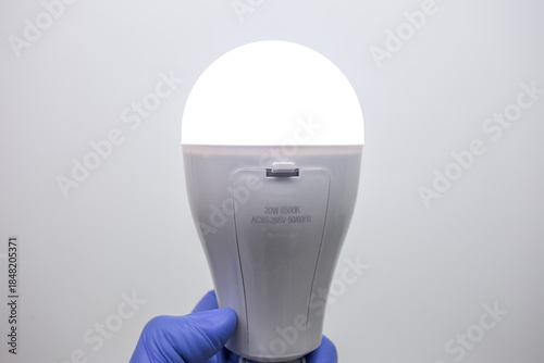 A person holds a switched-on LED light bulb with a battery compartment in his gloved hand; the LED light bulb operates autonomously from the battery.