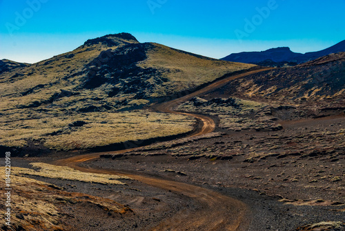 Winding dirt road through rugged volcanic highland landscape in Iceland with barren terrain and dramatic mountains