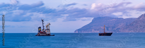 Sunken cargo ship and wreck salvage operation near rocky coastline