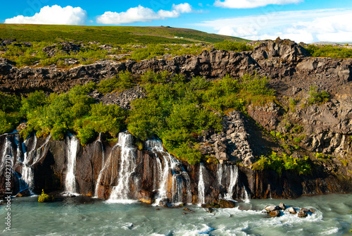 Hraunfossar is a unique Icelandic waterfall in West Iceland where clear, cold spring water seeps directly from under the Hallmundarhraun lava field, forming hundreds of small, delicate waterfalls.