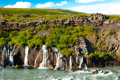 Hraunfossar is a unique Icelandic waterfall in West Iceland where clear, cold spring water seeps directly from under the Hallmundarhraun lava field, forming hundreds of small, delicate waterfalls.