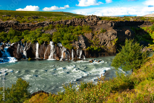 Hraunfossar is a unique Icelandic waterfall in West Iceland where clear, cold spring water seeps directly from under the Hallmundarhraun lava field, forming hundreds of small, delicate waterfalls.