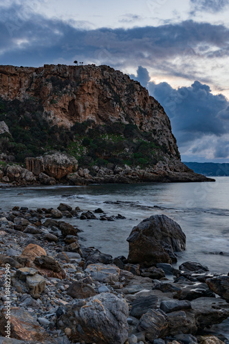 Rocky coastal cliff and calm sea under dramatic cloudy sky